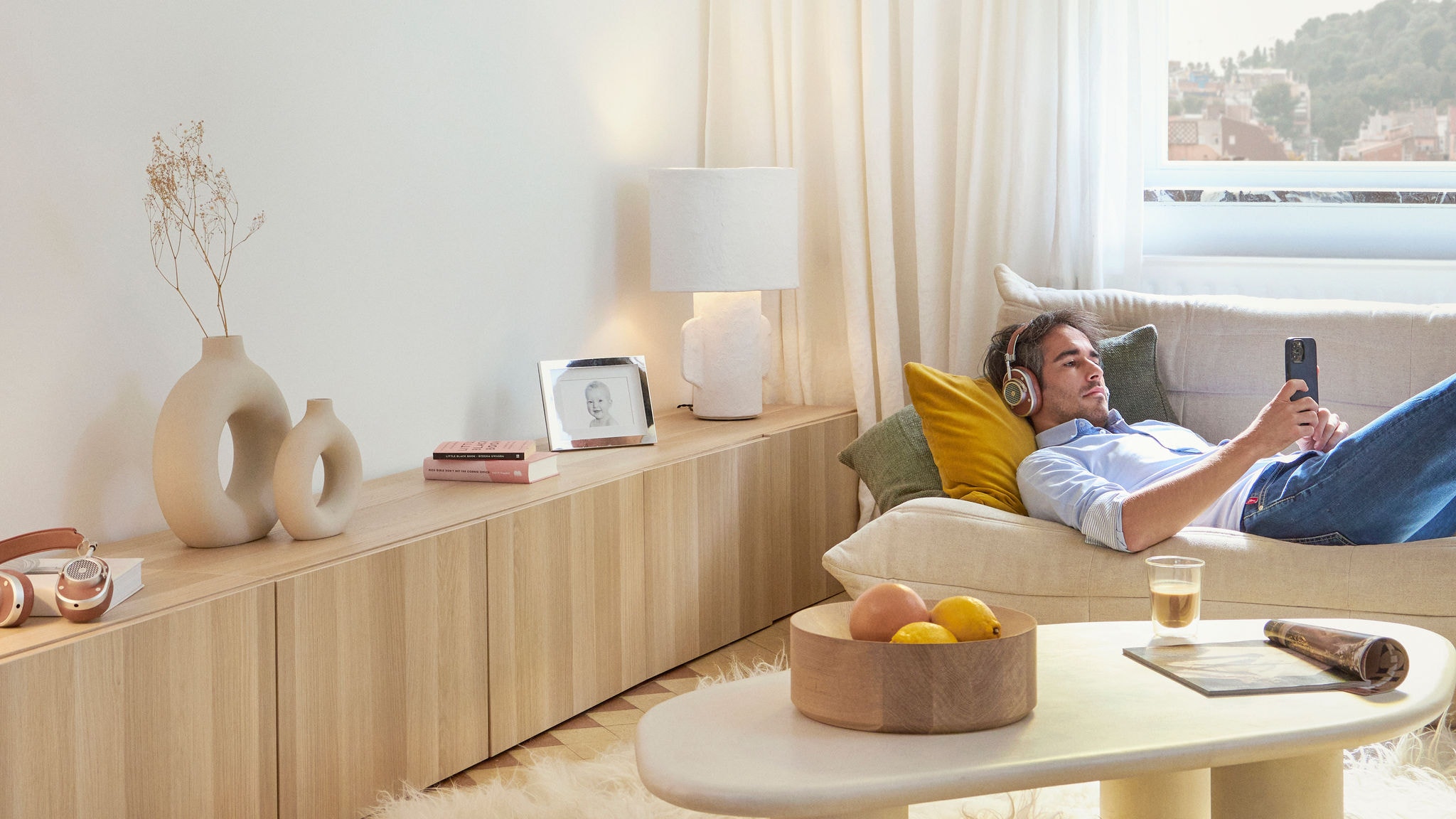 Relaxáló férfi a kanapén fekszik, és fejhallgatót viselve nézi telefonját a nappaliban