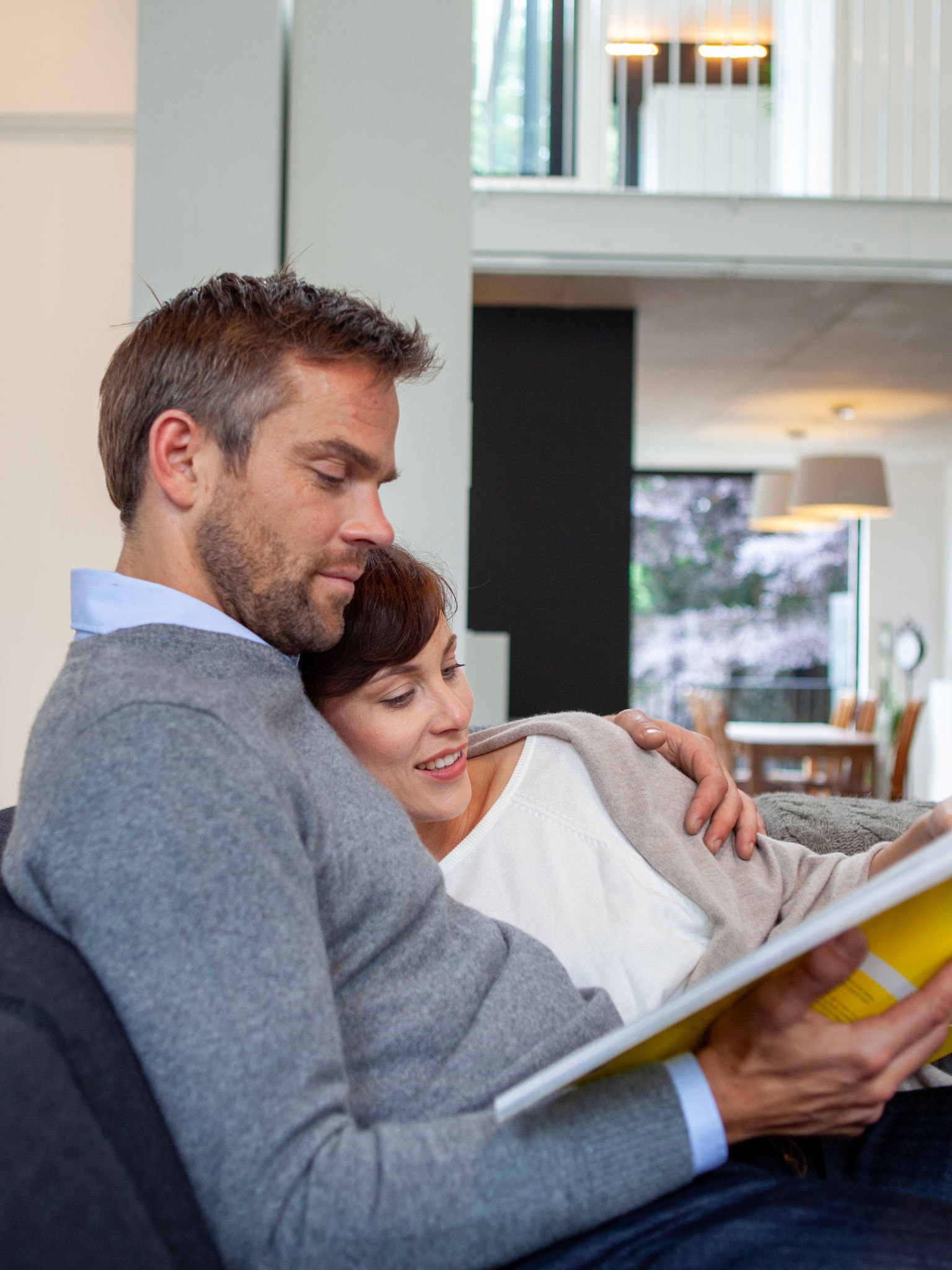 Ölelkező pár a kanapén könyvet olvas a tökéletes hőmérsékletű otthonában