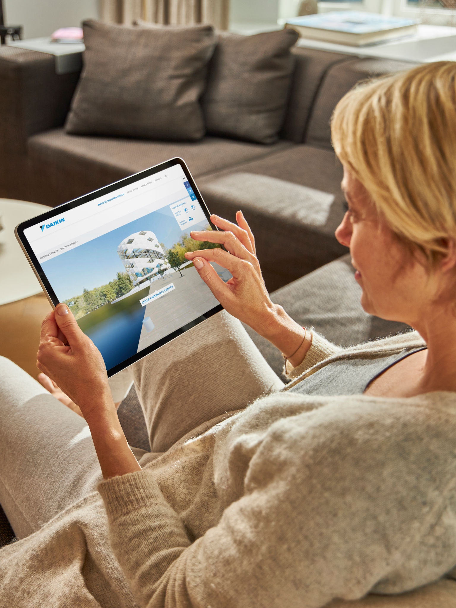 Egy nő a kanapén ülve nézi a klímákat tabletjén, a virtuális élményközpontban