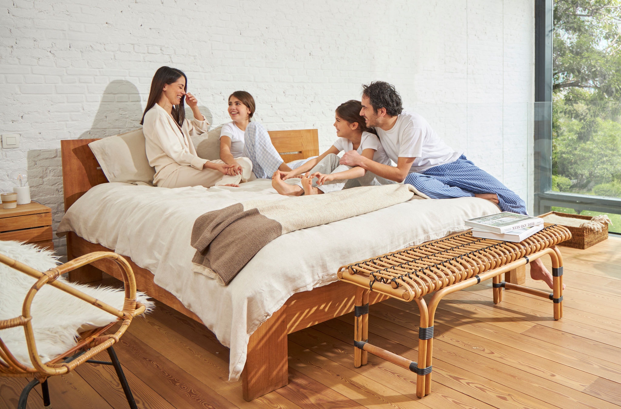 Egy nő és egy férfi ül egy ágyon két fiatal lánnyal lazán, nevetve és élvezik az egészséges levegőt.