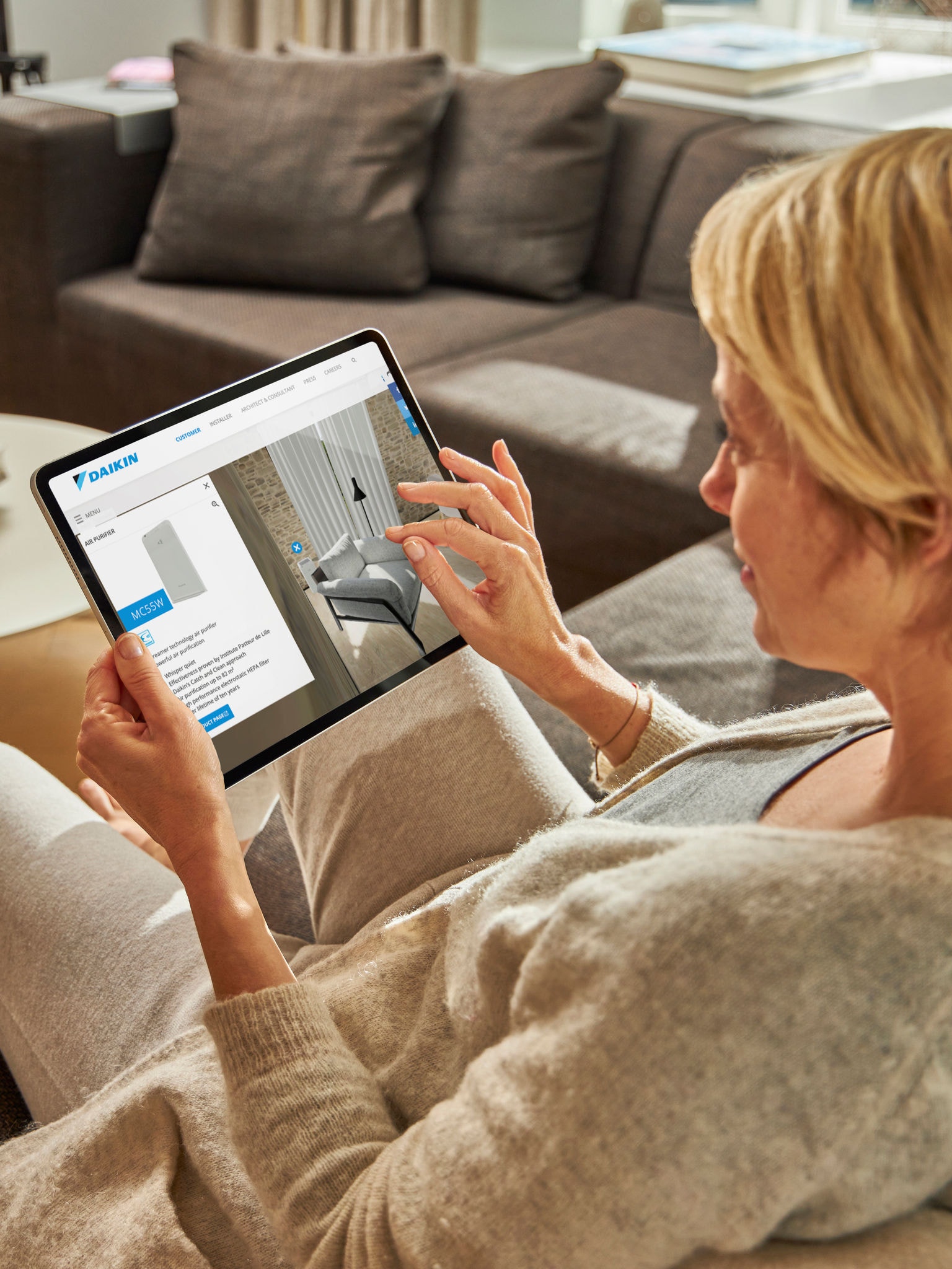 Egy nő a kanapén ülve nézi a klímákat tabletén, a virtuális élményközpontban