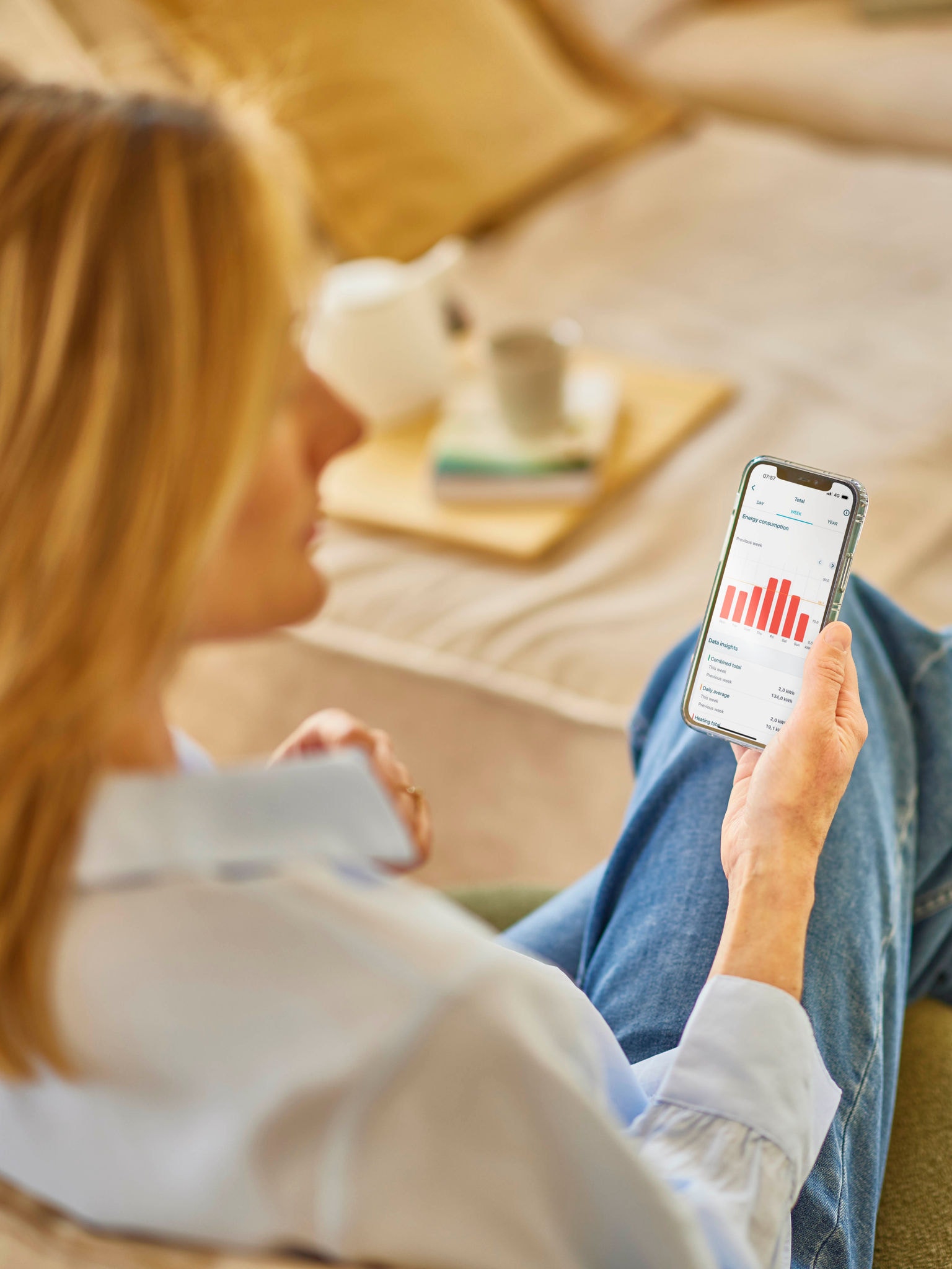 Szőke nő, aki telefonja egy alkalmazásán nézi az energiafogyasztását