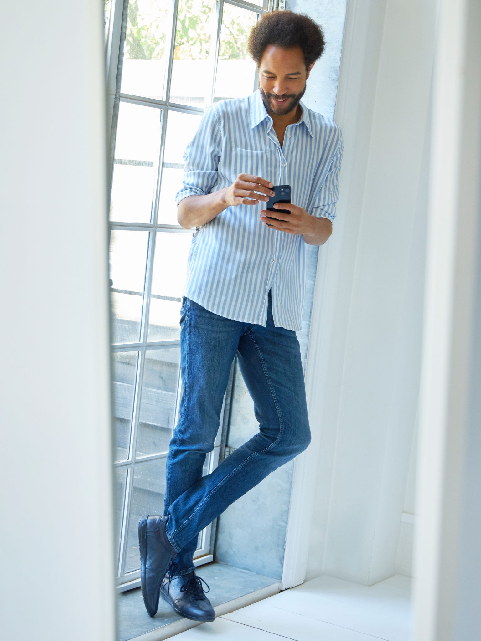 Ablak mellett álló férfi nézi okostelefonján a klímákat a virtuális bemutatóteremben.