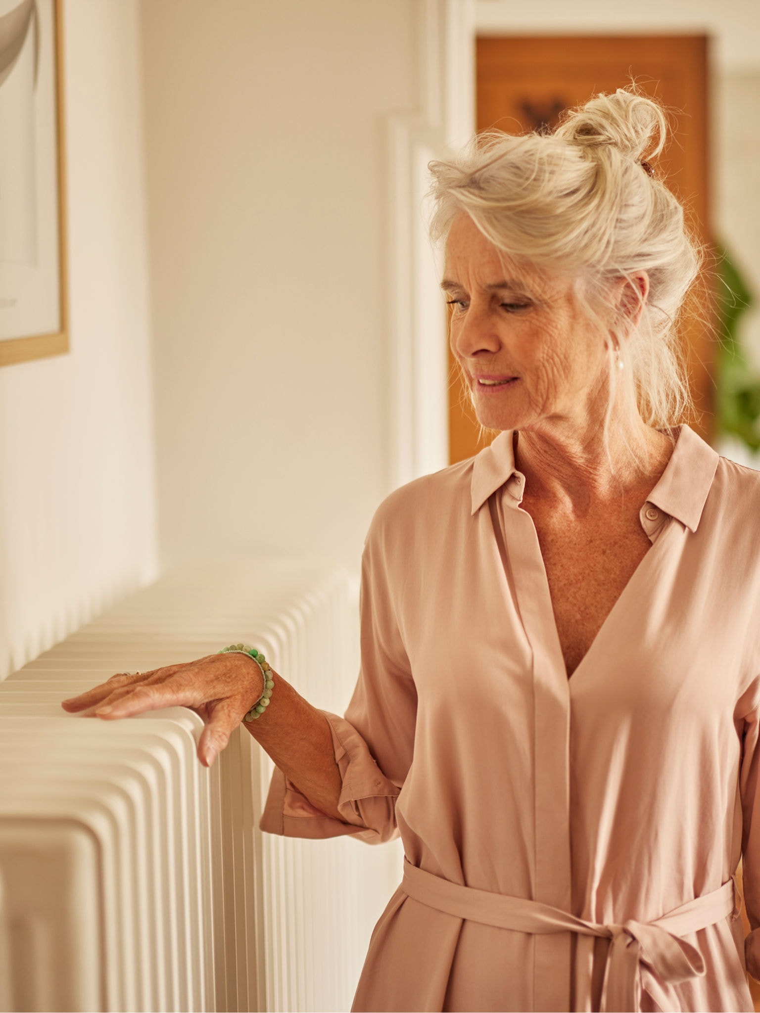 Egy nő a kezeit melegíti a levegő alapú hőszivattyúval társított radiátoron a hálószobában