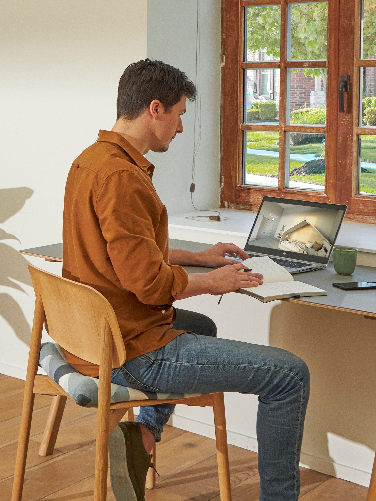 Ablak mellett álló férfi nézi laptopján a klímákat a virtuális bemutatóteremben.