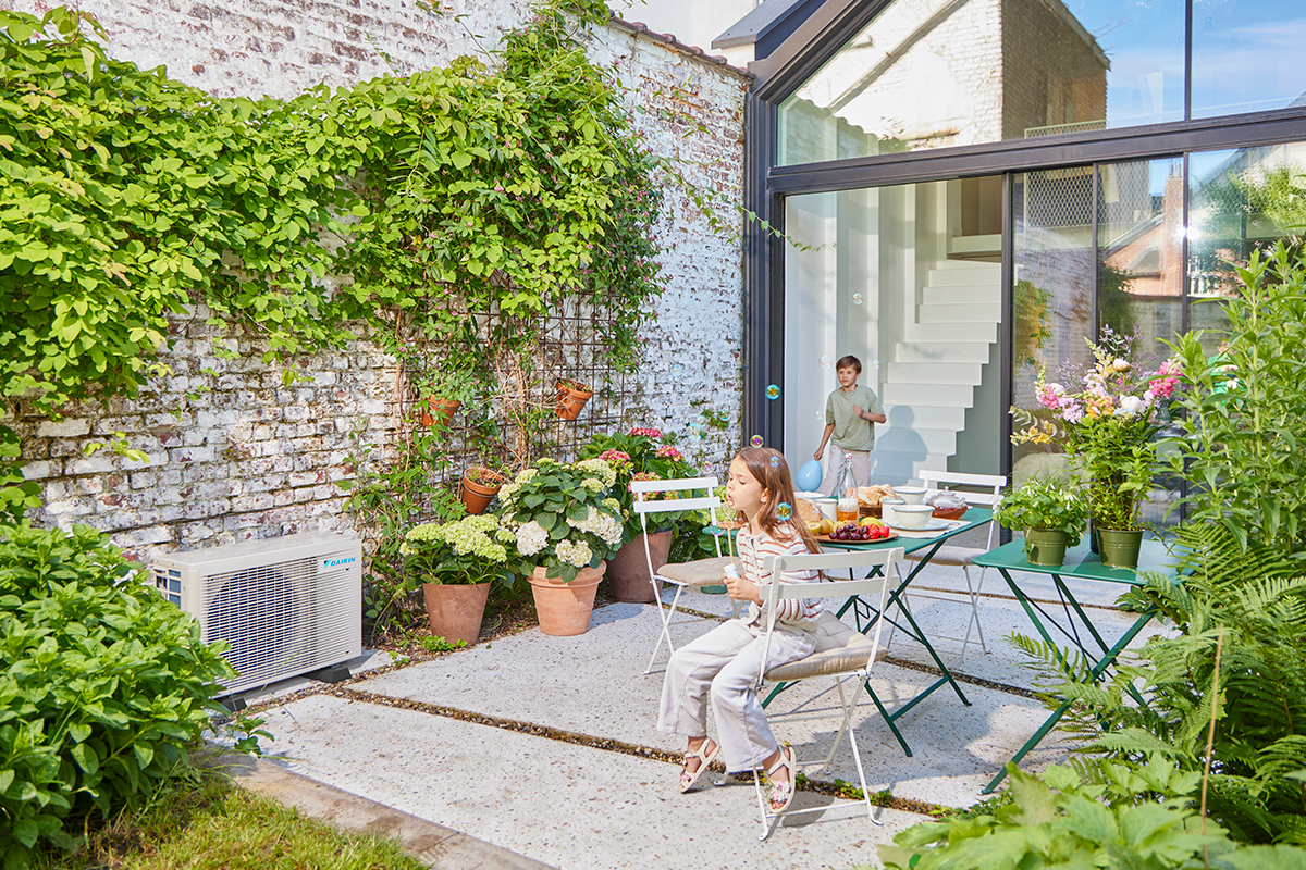 Gyerekek üveggolyóznak egy kerti teraszon egy kültéri hőszivattyú mellett
