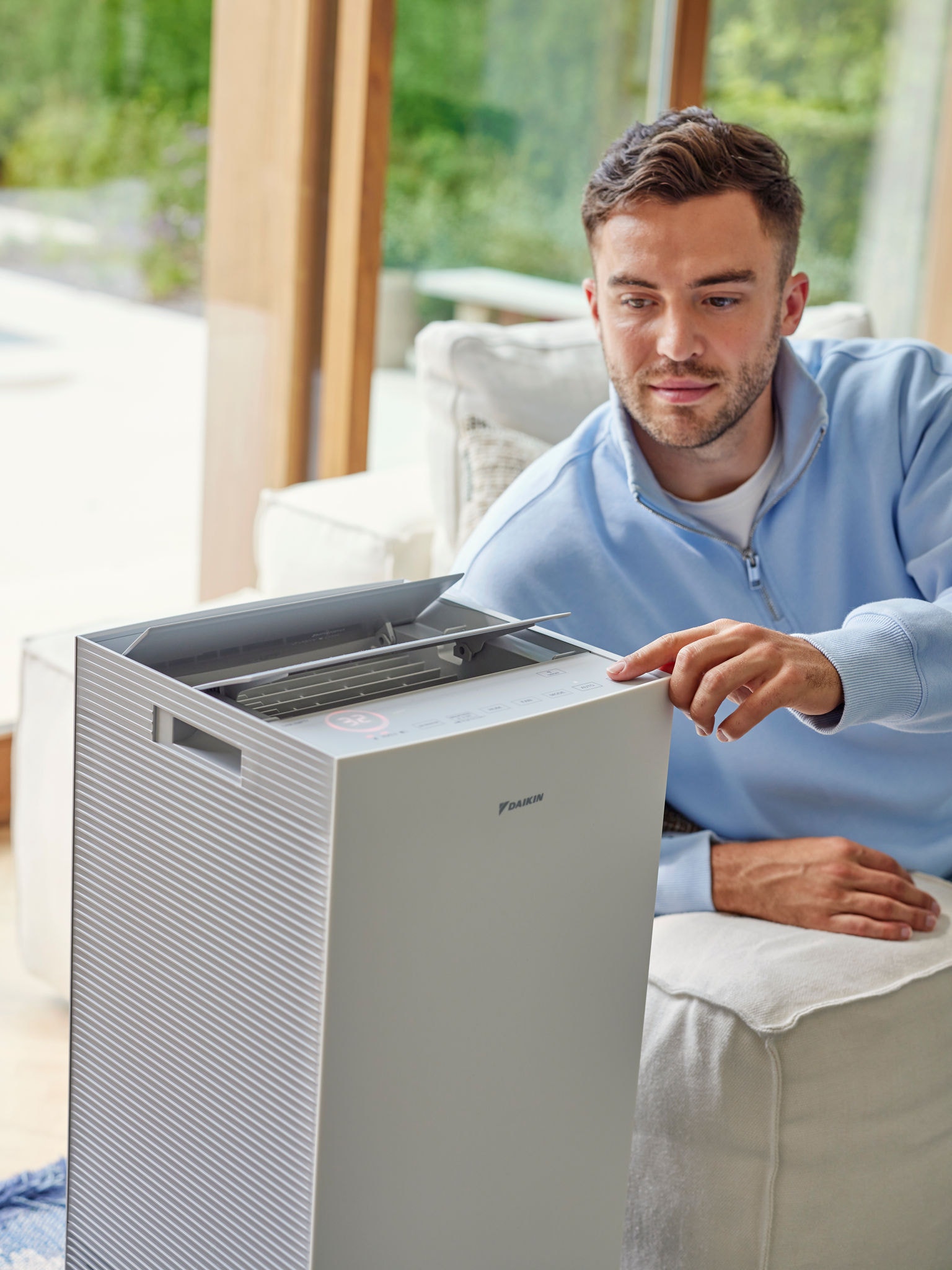 Férfi a nappaliban állítja be a Daikin légtisztítót, hogy csökkentse a macska allergének mennyiségét