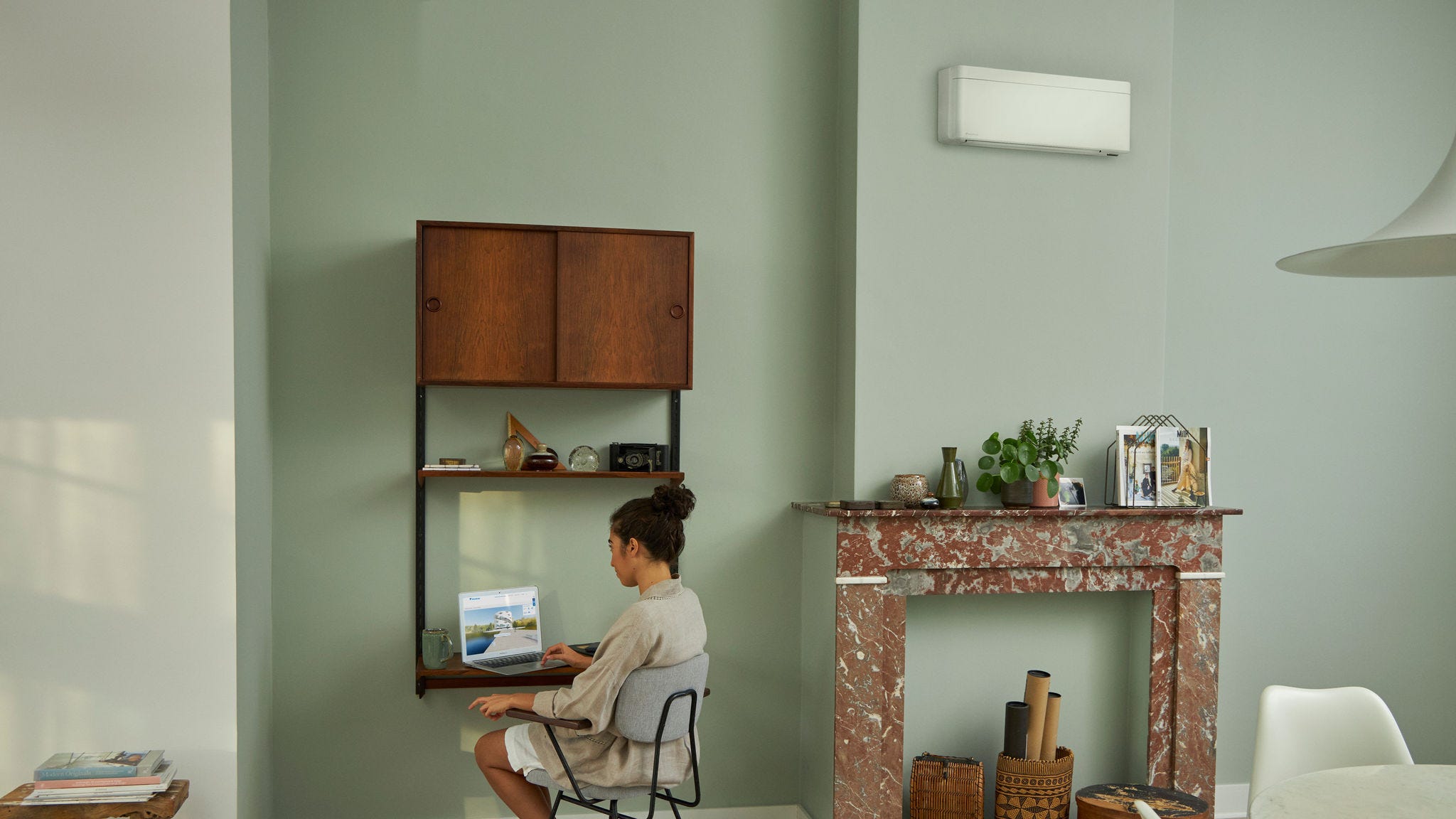 Egy nő a gyönyörű nappalijában elhelyezett kis asztalnál ülve a laptopján felkeresi a Daikin Virtuális Élményközpontot